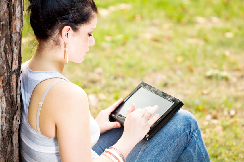 Frau im Grünen mit einem Tablet auf dem Schoß